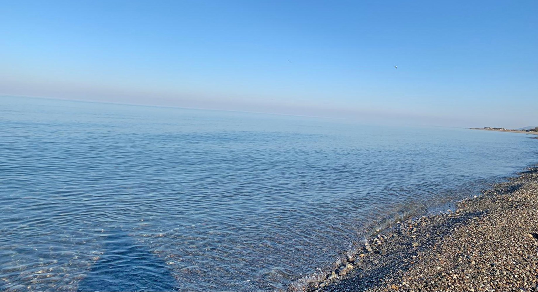Spiaggia con mare cristallino, rocce e ombrelloni colorati vista dall'alto.
