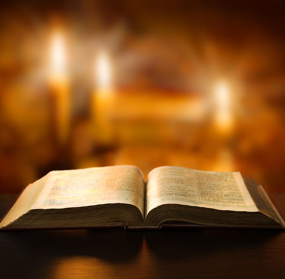 Un libro aperto su un tavolo, illuminato da due candele sullo sfondo.